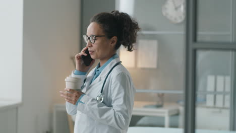 Female-Doctor-Holding-Coffee-and-Talking-on-Phone-at-Work